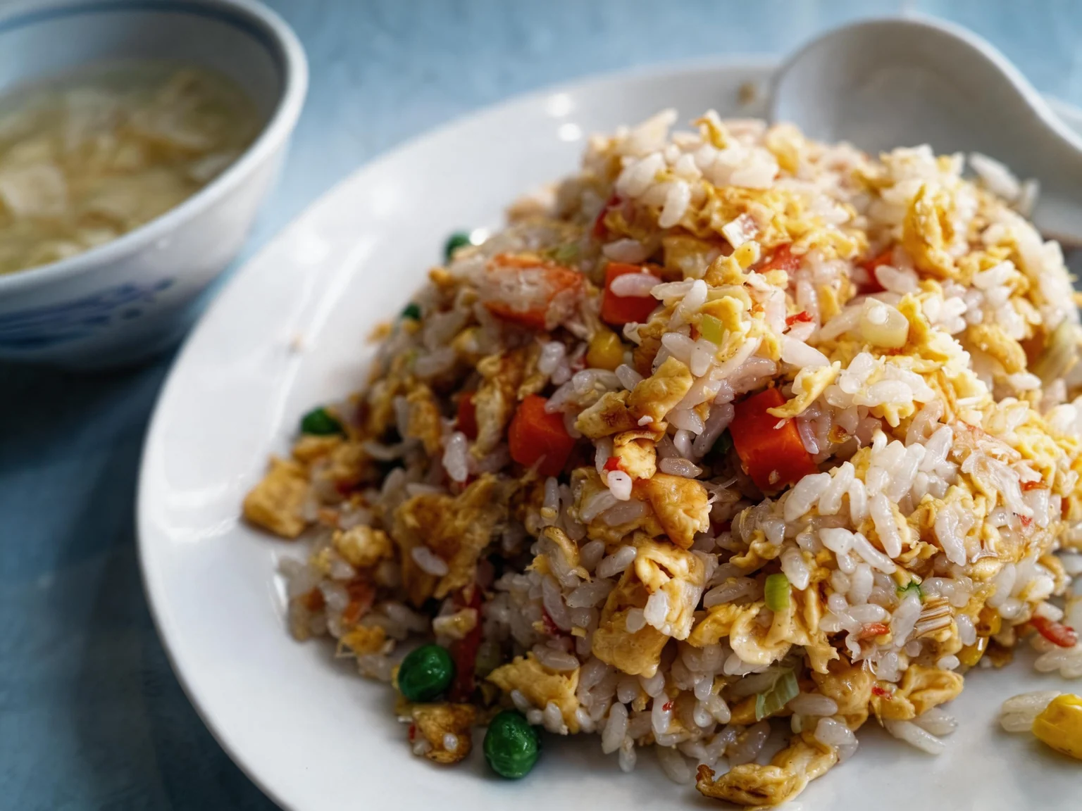 Cantonese rice. On a white plate, with a bowl beside it.